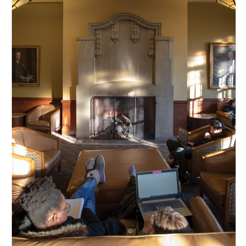 two people studying on a couch facing a fireplace