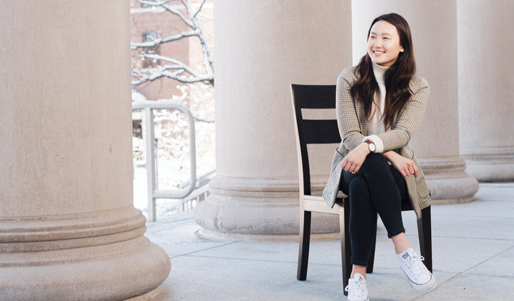 Shannon Kang sitting on a chair next to pillars